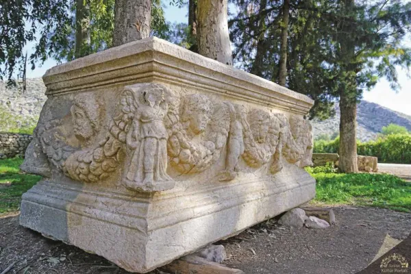 Antik bir lahit, detaylı figürler ve doğal yeşilliklerle çevrili, tarihi atmosfer.