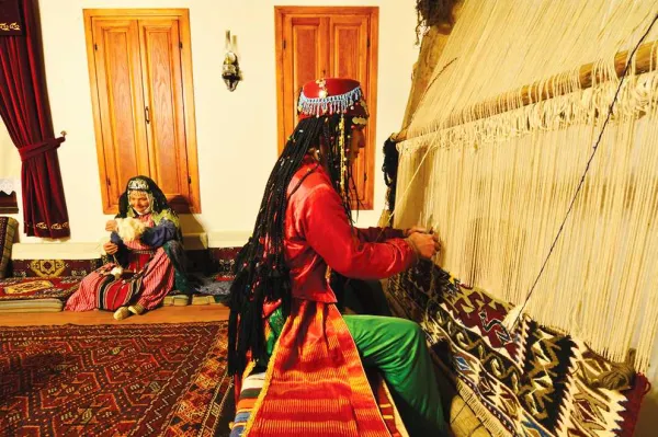 Geleneksel el sanatı sergileyen sıcak bir ortamda kadın dokuma yapıyor.