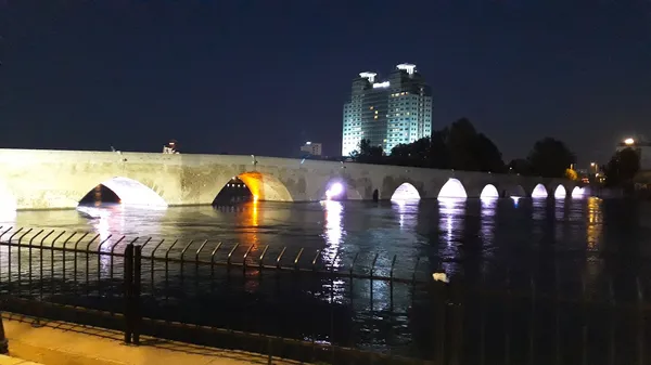 Taş köprü ve modern binalar ile huzurlu gece manzarası.