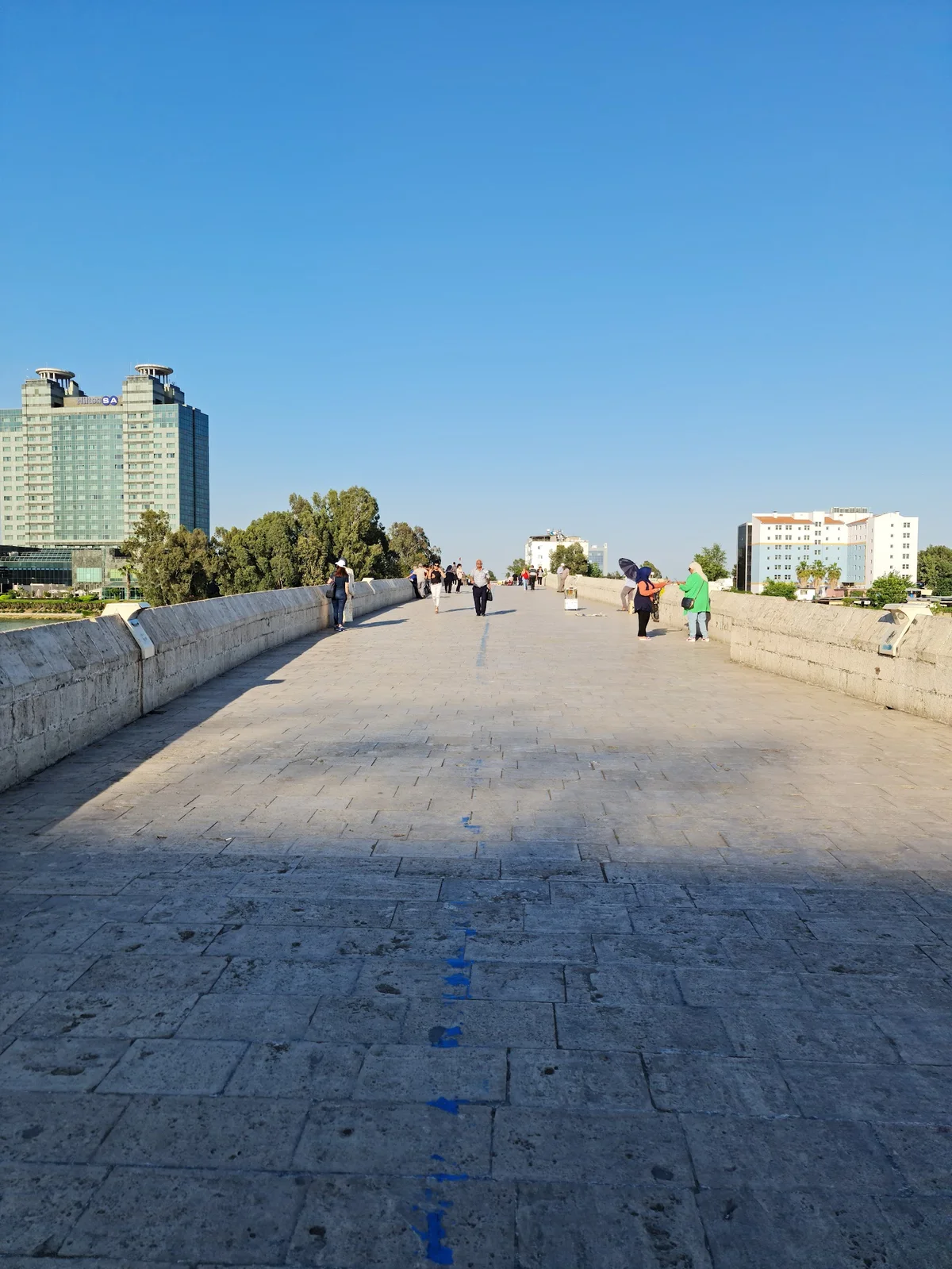 Taş Köprü Yürüyüş Yolu ve Sakin Atmosfer Taş kaplama yürüyüş yolu, ağaçlar ve modern otel manzarası.