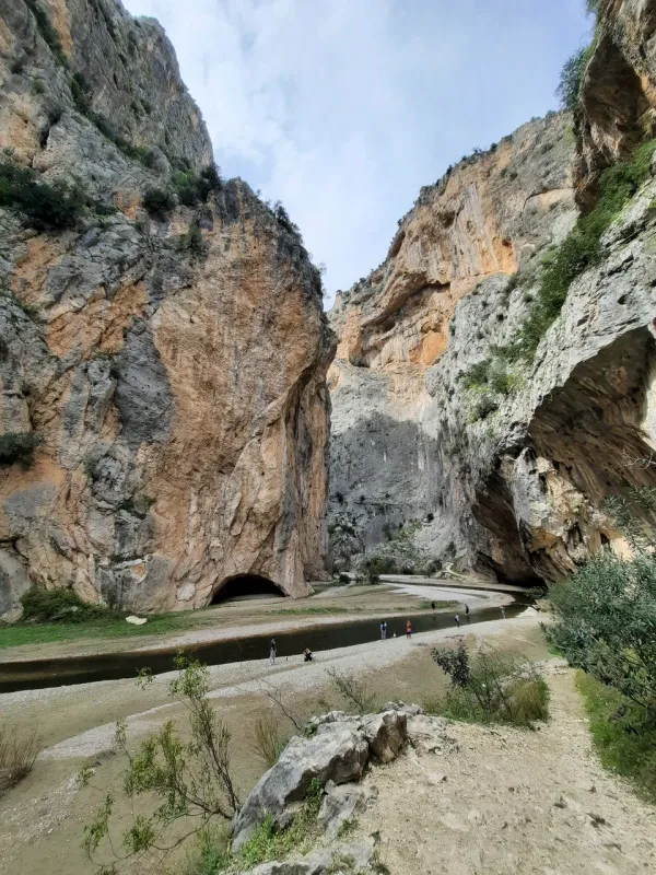Dik kayalıklarla çevrili Kapıkaya Kanyonu'nda yürüyüş yapan insanlar ve akan dere.