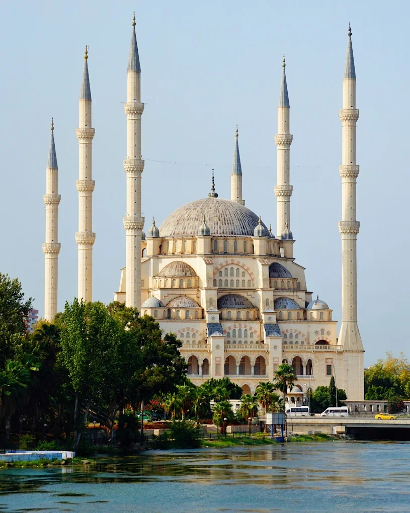 Beyaz taşlardan inşa edilmiş büyük bir cami ve beş minaresi, su yansımasında görünüyor.