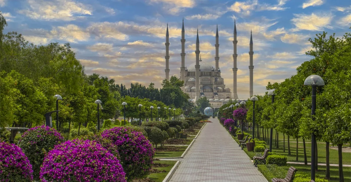 Sabancı Merkez Camii'nin Etkileyici Güzelliği Geniş park alanında altı minareli Sabancı Merkez Camii ve renkli çiçeklerle dolu peyzaj.