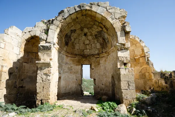 Antik yapının kalıntıları, mavi gökyüzü ve yeşil bitkilerle çevrili.