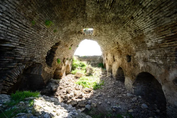 Geniş taş yapı kalıntısının içi, yüksek kemerli tavan ve yeşil bitkilerle doğal bir görünüm sunuyor.