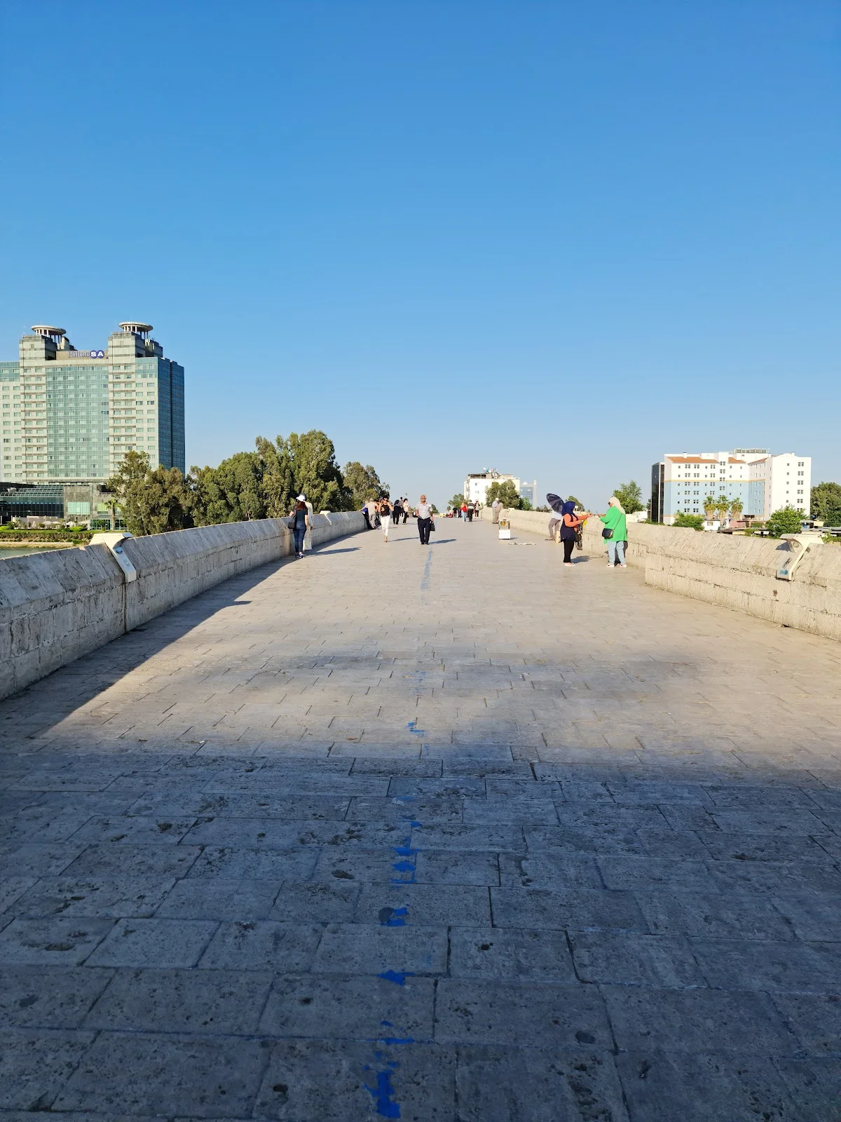 Misis Höyük'teki taş köprüde yürüyen insanlar ve modern binalar. Misis Höyük'teki taş köprüde yürüyen insanlar ve modern binalar.