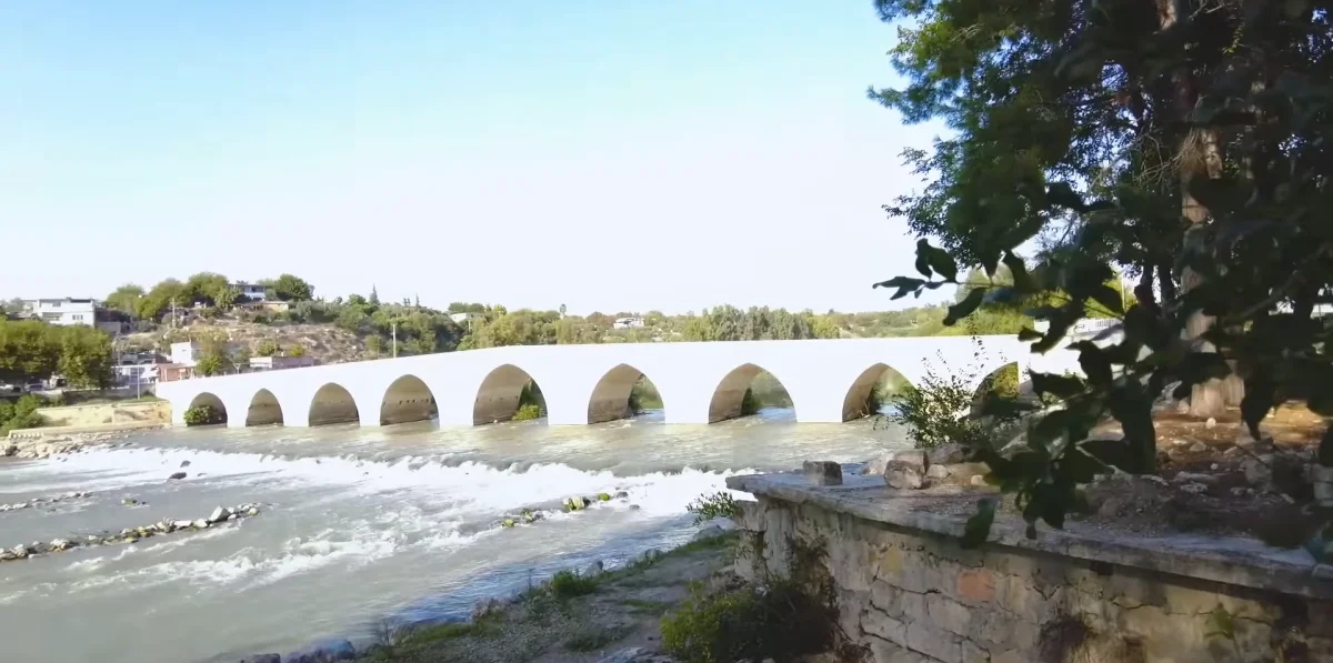Kemerli beyaz köprü, akıcı nehir ve yeşil ağaçlarla huzurlu bir manzara sunuyor.