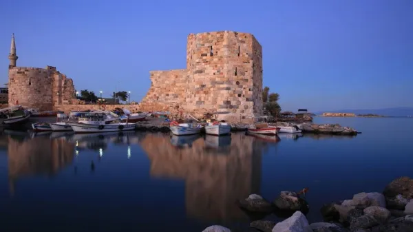 Tarihi bir kale ve su kenarında küçük tekneler, huzurlu bir akşamüstü atmosferi sunuyor.