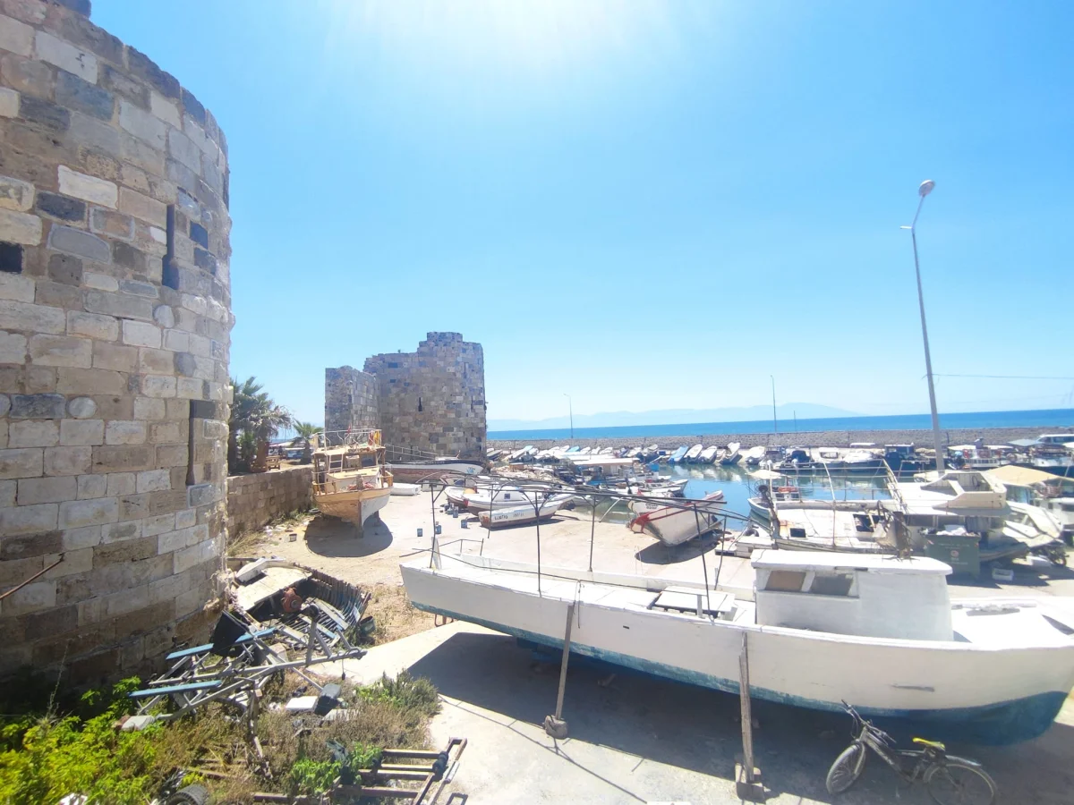 Ayas Antik Kenti'nde Deniz Kenarında Marina Manzarası Deniz kenarındaki marina, yuvarlak kule ve yıkık duvar ile birlikte canlı bir atmosfere sahip.