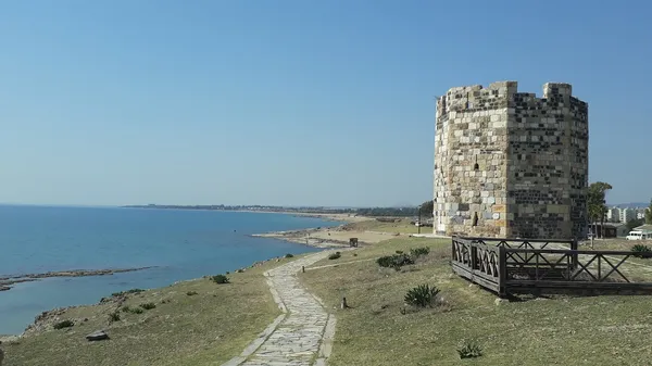 Ayas Antik Kenti'nde tarihi kule ve sakin deniz manzarası.
