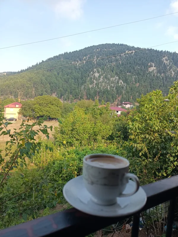 Beyaz fincan içinde kahve, yeşil dağ manzarası ve renkli evler