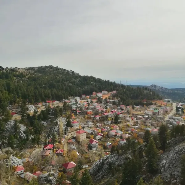 Dağlarla çevrili, renkli çatılı evlerin yer aldığı huzurlu bir kasaba manzarası.