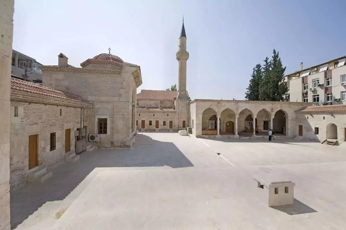Yağ Camii: Tarihi Yapının Göz Alıcı Avlusu Yağ Camii avlusunda taş zemin, yüksek minare ve çevredeki taş yapılar.