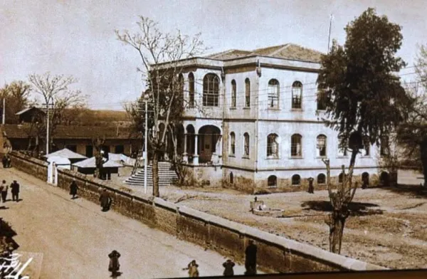 İki katlı tarihi bina, kayrak taşlı merdivenler ve çevresindeki ağaçlarla kış manzarası.