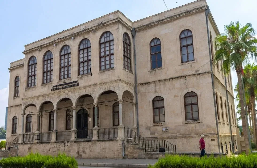 Adana Tarihi Kız Lisesi: Mimari Güzellik Açık renkli taşlardan yapılmış tarihi bina palmiyelerle çevrili bahçede yer alıyor.