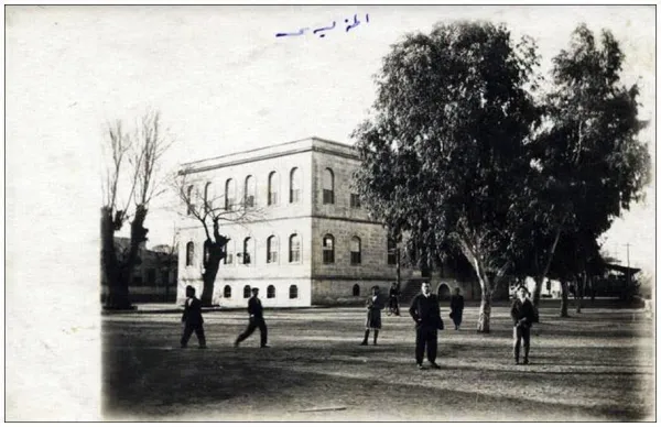 Tarihi taş bina ve ağaçların bulunduğu açık alanda yürüyüş yapan insanlar.