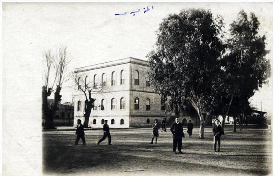 Adana Tarihi Kız Lisesi: Geçmişin İzleri Tarihi taş bina ve ağaçların bulunduğu açık alanda yürüyüş yapan insanlar.