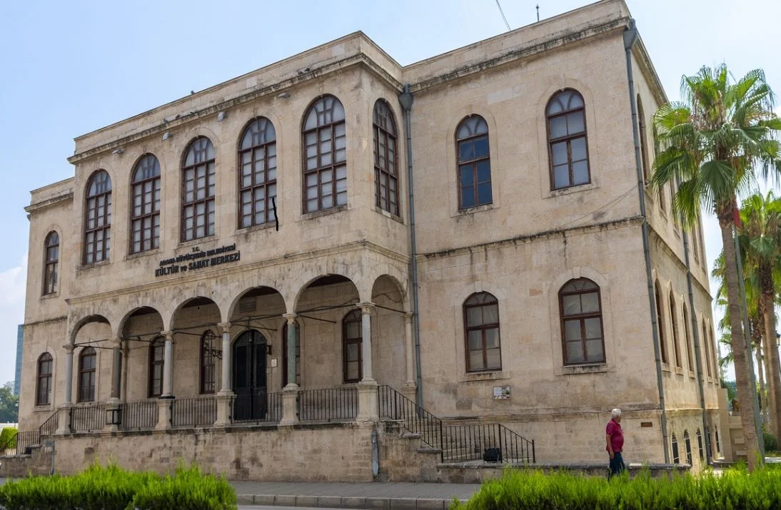 Adana Tarihi Kız Lisesi'nin Büyüleyici Görünümü Tarihi yapının yuvarlak pencereleri ve geniş merdiveni, palmiye ağaçlarıyla çevrili.