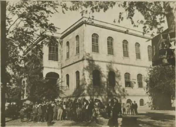 Büyük tarihi binanın önünde toplanmış kalabalık grup, klasik mimari detaylar ve yeşil ağaçlar.