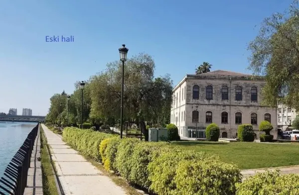 Yeşil park alanında yürüyüş yolu ve tarihi bina, mavi gökyüzüyle huzurlu bir atmosfer sunuyor.