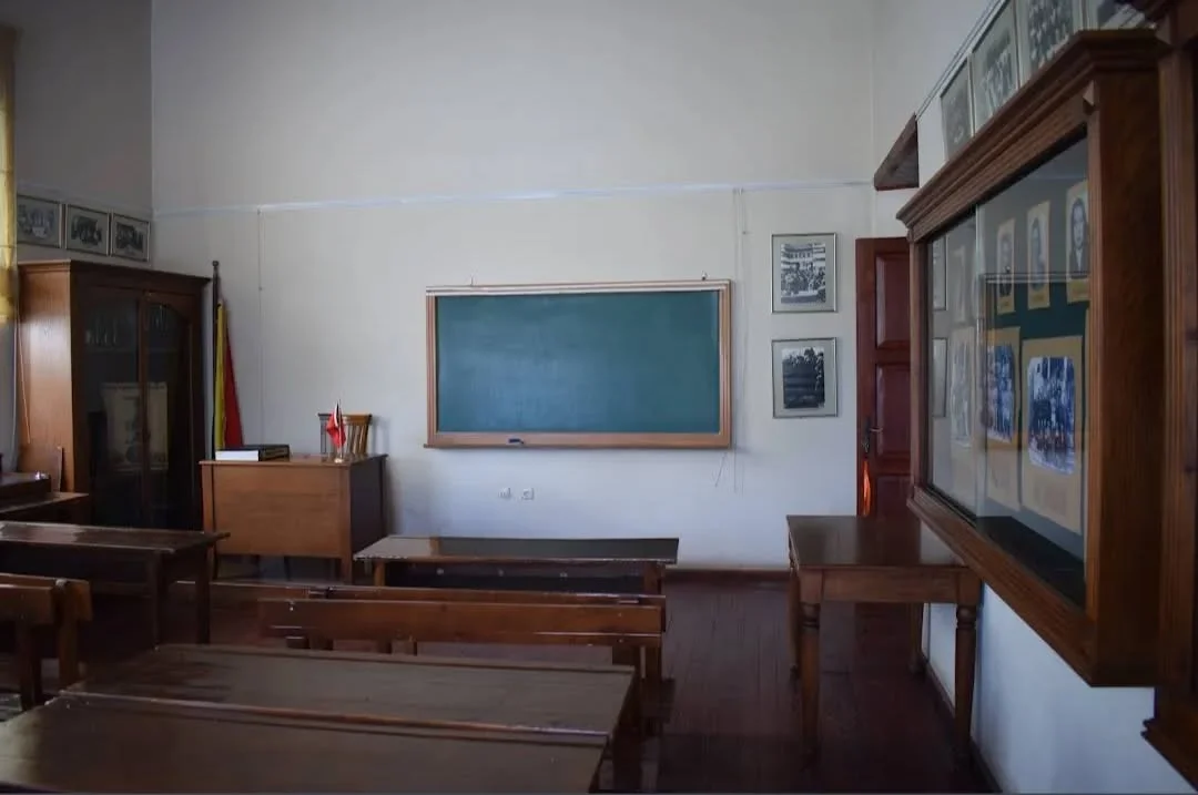 Adana Tarihi Kız Lisesi Sınıf Ortamı Klasik bir sınıf ortamında yeşil tebeşir tahtası ve çerçeveli fotoğraflar yer alıyor.