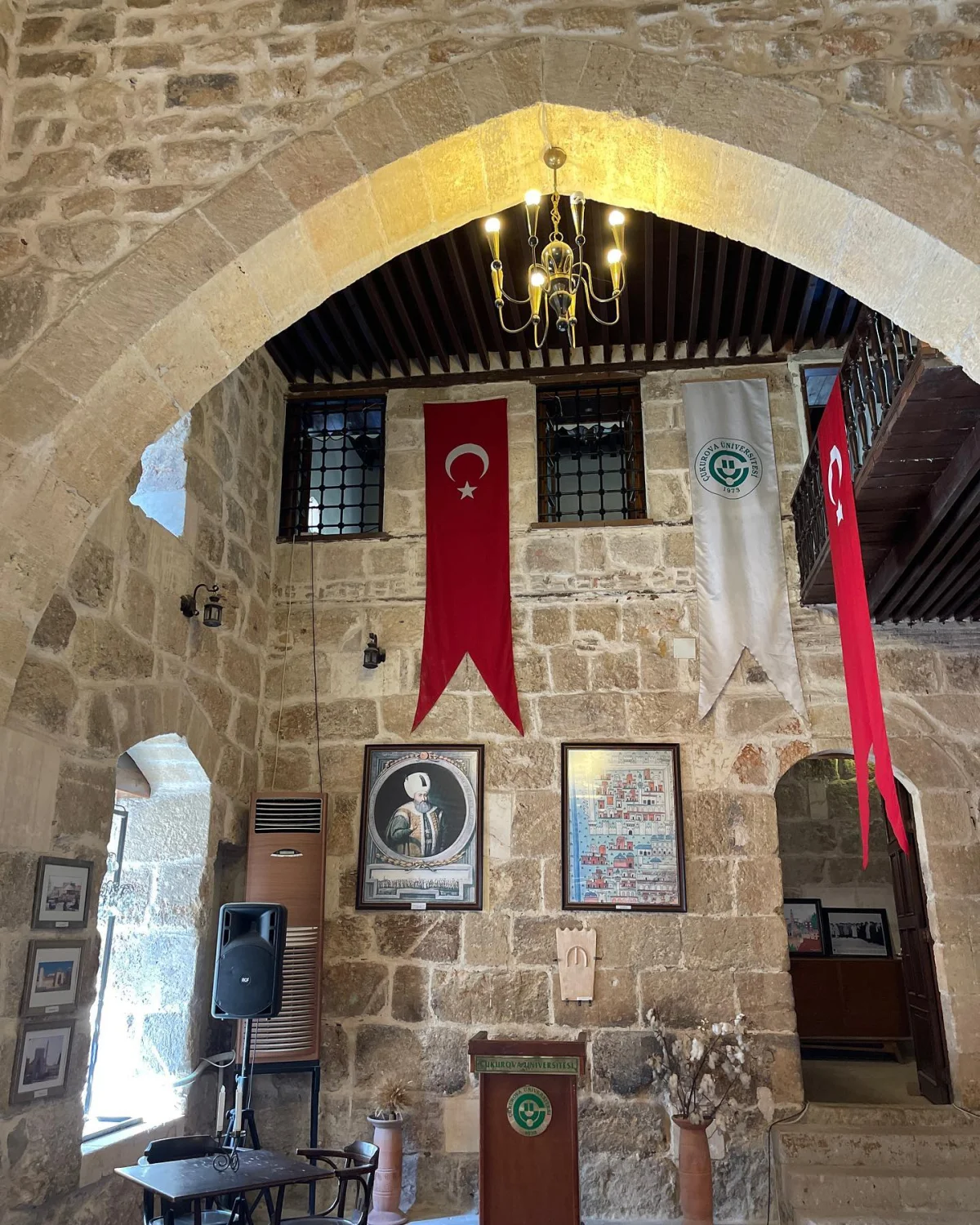 Tarihi bir binanın iç mekanı, taş duvarlar ve klasik avize ile dikkat çekiyor.