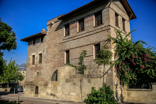 Tarihi Ramazanoğlu Konağı, yeşil ağaçlar ve pembe çiçeklerle çevrili.