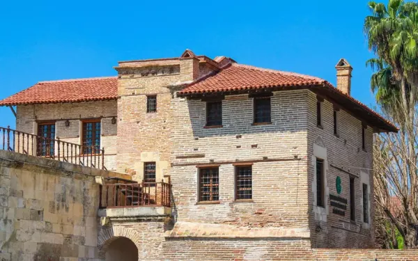 Tarihi Ramazanoğlu Konağı'nın tuğla ve taş cephesi, kırmızı kiremitli çatı ve yeşil palmiyelerle çevrili.