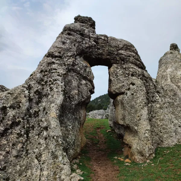 Büyük taşların arasında yürüyüş yolu ve yeşil bitki örtüsü ile kaplı doğal alan.
