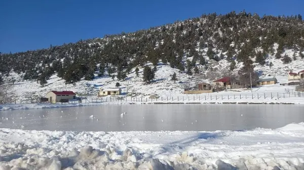 Karlı alanda ince buz tabakası ile kaplı göl ve karla örtülü evler