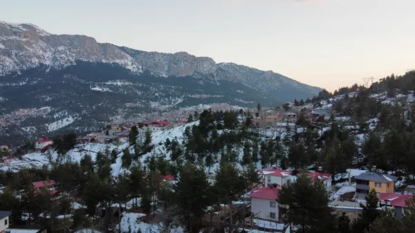 Karlı dağların arasında kırmızı çatılı evler ve yeşil ağaçlar