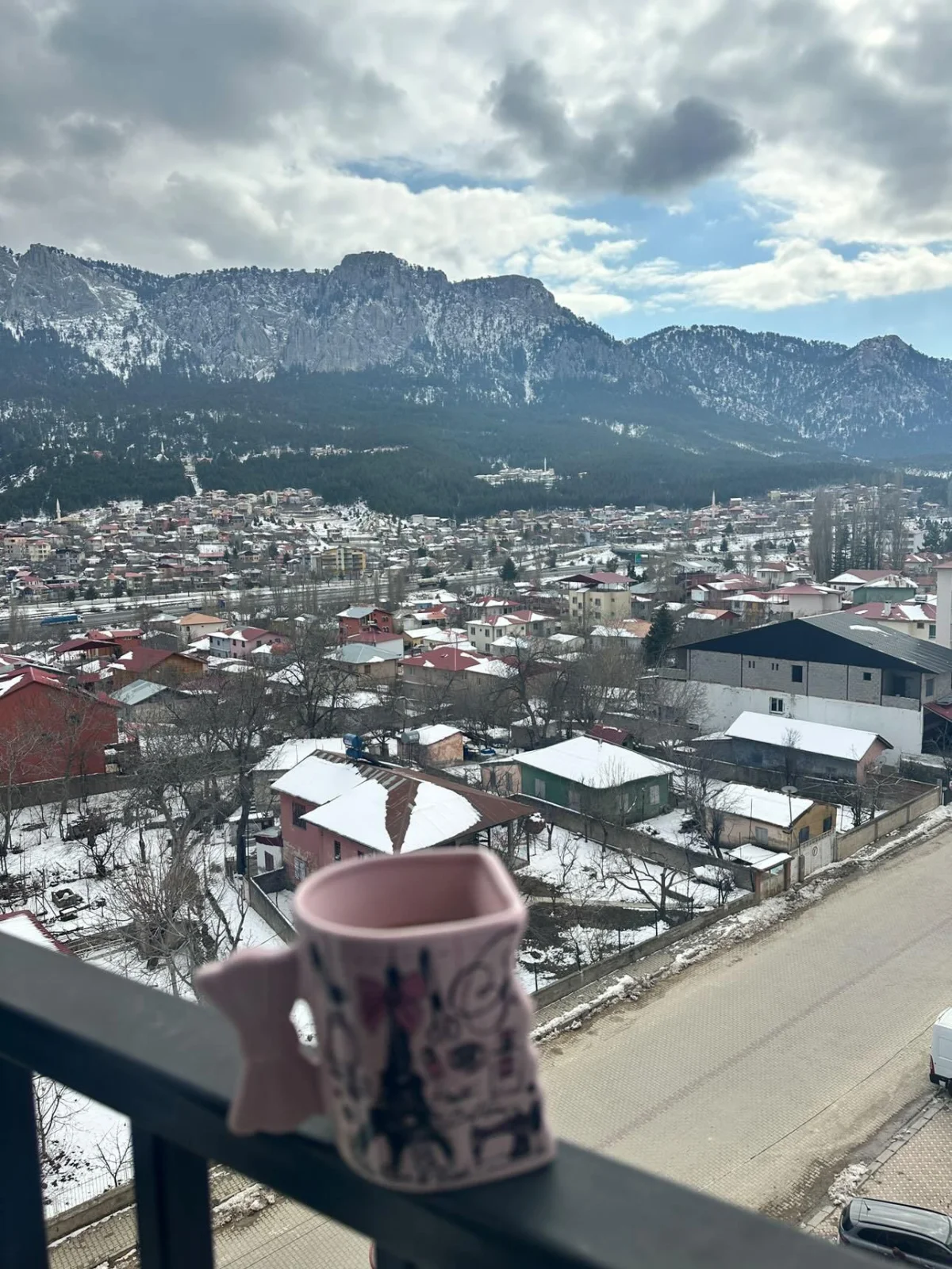 Karla kaplı dağ manzarası ve renkli evlerin bulunduğu sakin bir yayla görüntüsü.