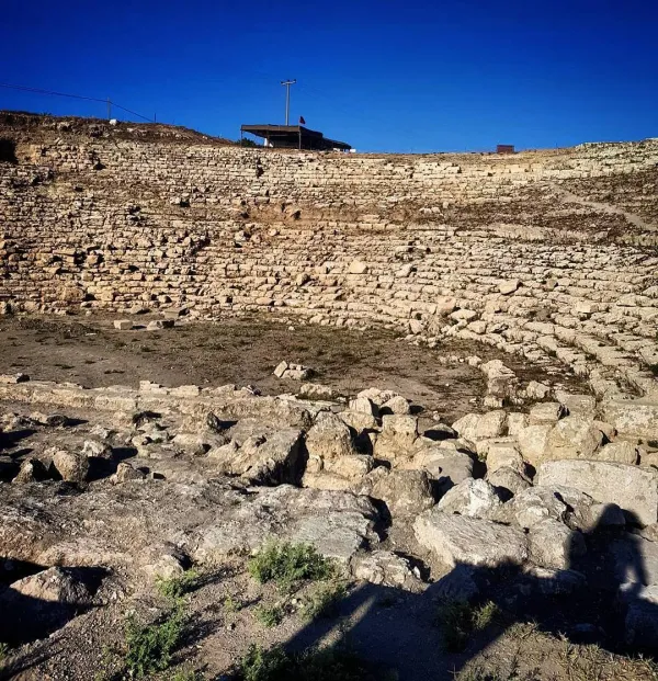 Antik amfitiyatronun kalıntıları, mavi gökyüzü ve bayrak ile birlikte.