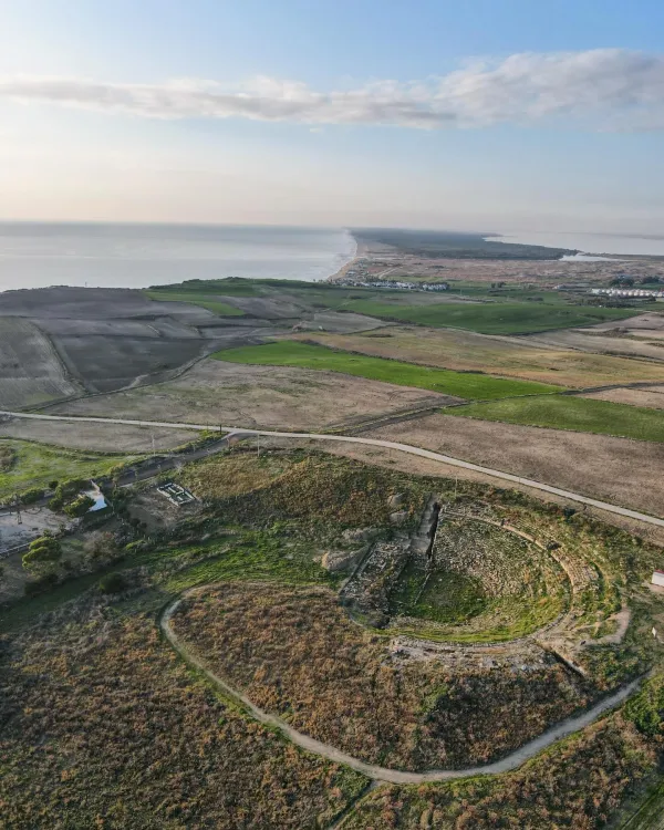Deniz kıyısında eski yapının kalıntıları ve yeşil tarım alanları.