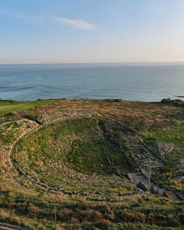 Yeşil bitki örtüsüyle çevrili antik tiyatro ve mavi deniz manzarası