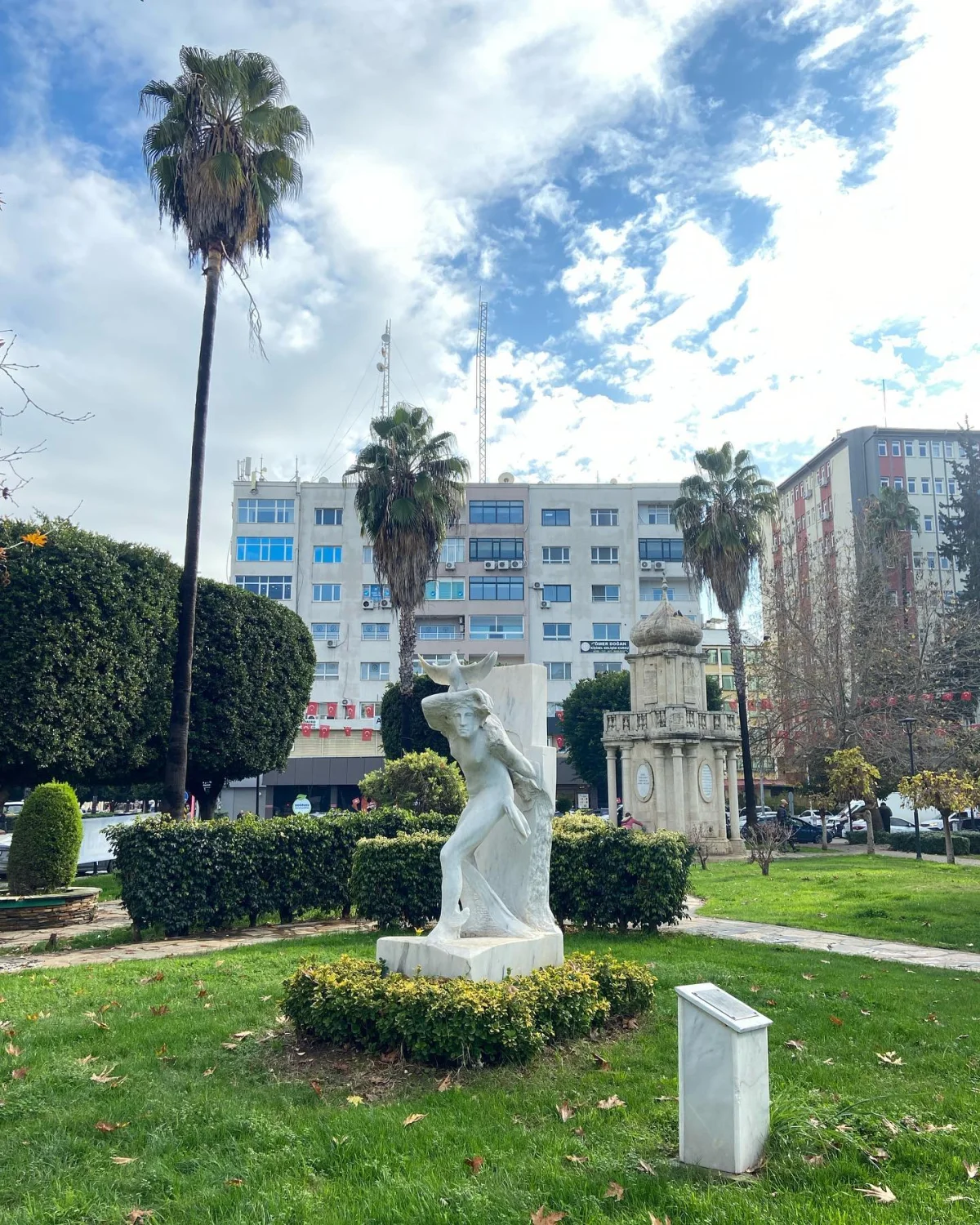 Modern binaların arka planında palmiyelerle çevrili beyaz heykel ve tarihi çeşme