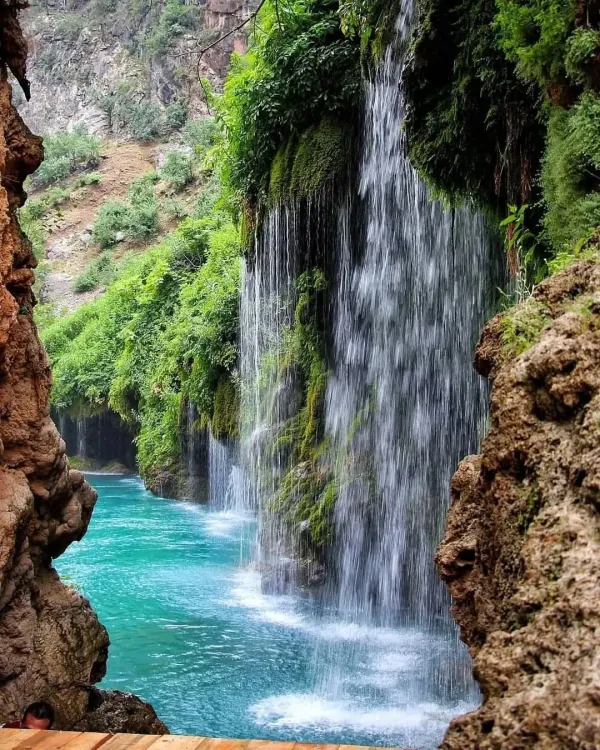 Yemyeşil bitki örtüsüyle çevrili doğal alanda turkuaz bir gölete düşen şelale.