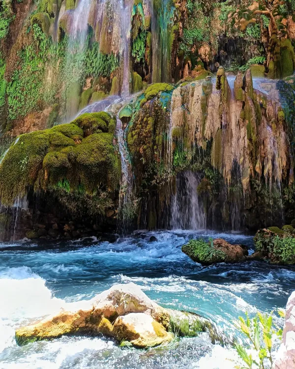 Yeşillikler ile çevrili kayalardan akan şelaleler ve berrak mavi su.