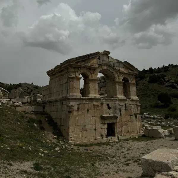 Antik yapının kalıntıları, büyük kemerli pencereler ve yeşil tepe arka planda.