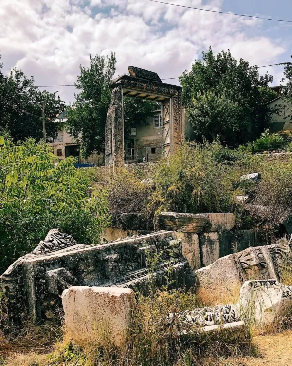 Taş bloklar ve yazılarla süslenmiş tarihi kalıntılar, yeşil bitki örtüsüyle çevrili.