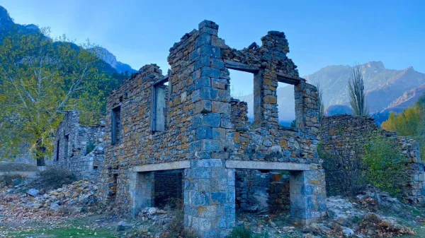Dağlarla çevrili terkedilmiş taş yapı, sararmış ağaçlar ve gün doğumu manzarası.