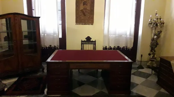 Koyu ahşap masa ve işlemeli sandalye ile tarihi bir iç mekan görünümü.