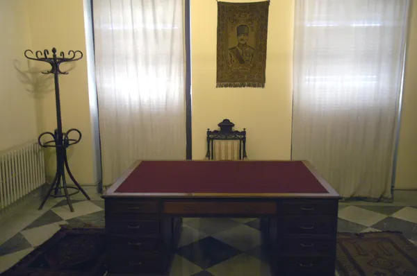 Sade bir odada büyük masa, klasik iskemle ve asılı resim ile tarihi bir atmosfer sunuyor.