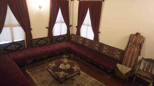 Koyu kırmızı perdeler ve işlemeli yastıklarla döşenmiş geniş oturma grubu.