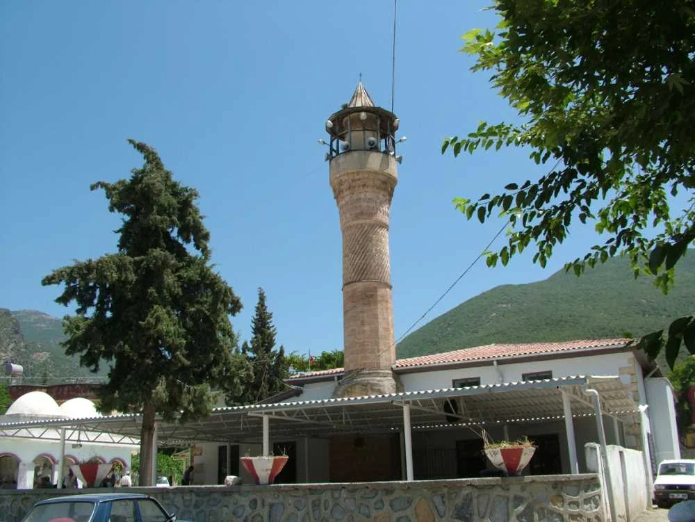 Ağcabey Cami - Osmaniye'nin Tarihi Mirası ve Doğal Güzellikleri Keşfetmeye Hazır mısınız? Ağcabey Camii minaresi, güneşli bir günde yeşil ağaçlarla çevrili, huzurlu bir atmosfer sunuyor.