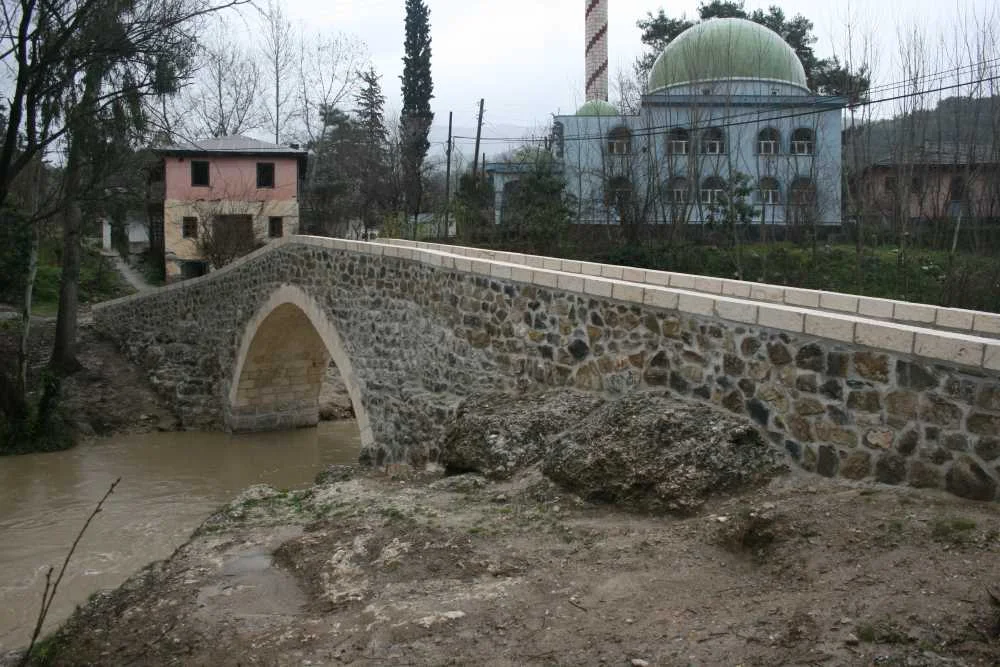 Gaffarlı Taş Köprü - Doğal ve Tarihi Güzellik: Yeşillikler ve Cami Manzarası! Gaffarlı Taş Köprü, yeşil kubbeli cami ile doğal manzara, hafif bulutlu bir atmosfer.