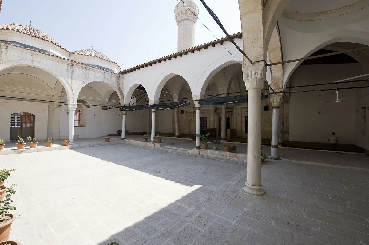 Hasan Ağa Camii'nin huzur veren avlusu: Osmanlı'nın zarafeti! Hasan Ağa Camii avlusunda ince sütunlarla desteklenen kemerler ve dinlenen bir kişi.
