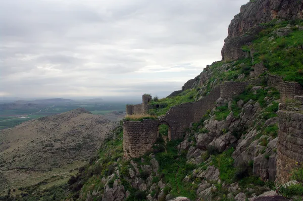 Yeşil dağlar arasında yer alan, taşlardan inşa edilmiş kalıntı yapının görüntüsü.