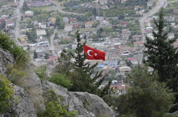 Yeşil ağaçlar arasında dalgalanan Türk bayrağı ve dağlık yerleşim manzarası.