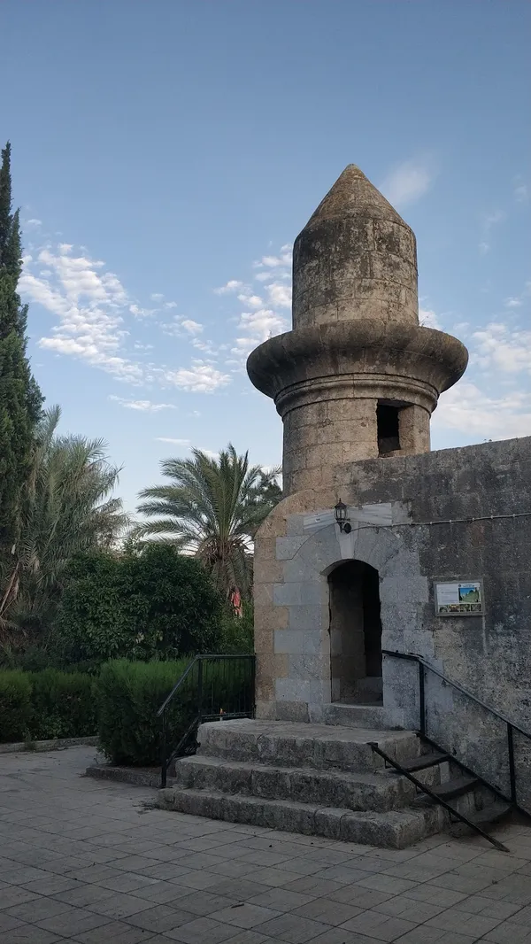 Eski taş kulesi ve yanında tarihi yapı, yeşil ağaçlarla çevrili.